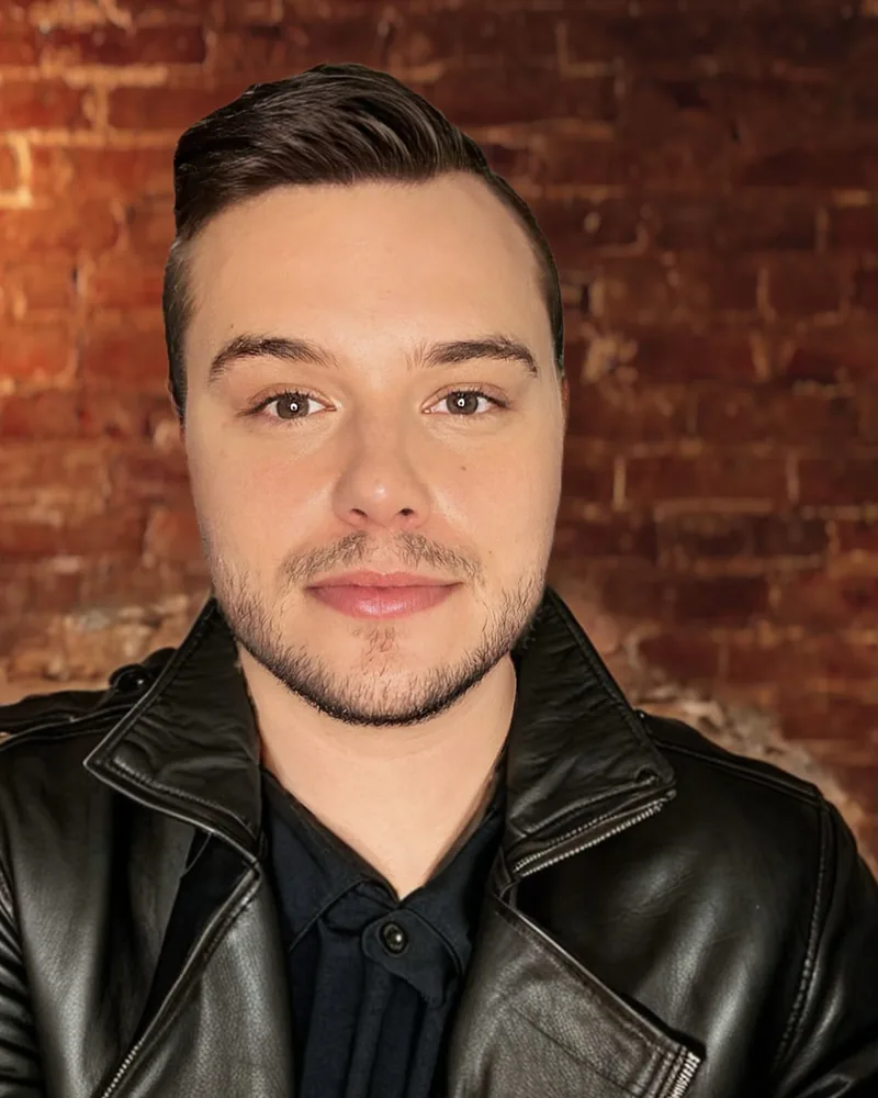 Jeremy Bish headshot in a black leather jacket in front of a brick wall